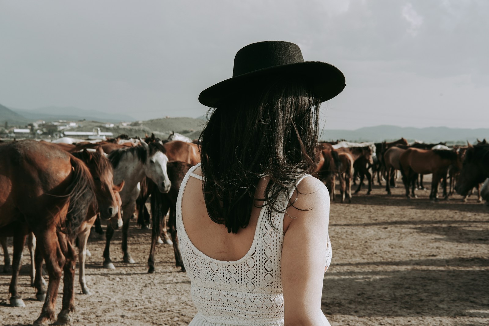 a woman wearing a hat standing in front of a herd of horses